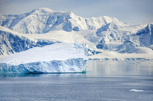 Iceberg flottant devant une chaîne de montagnes enneigées, illustrant les enjeux du changement climatique.
